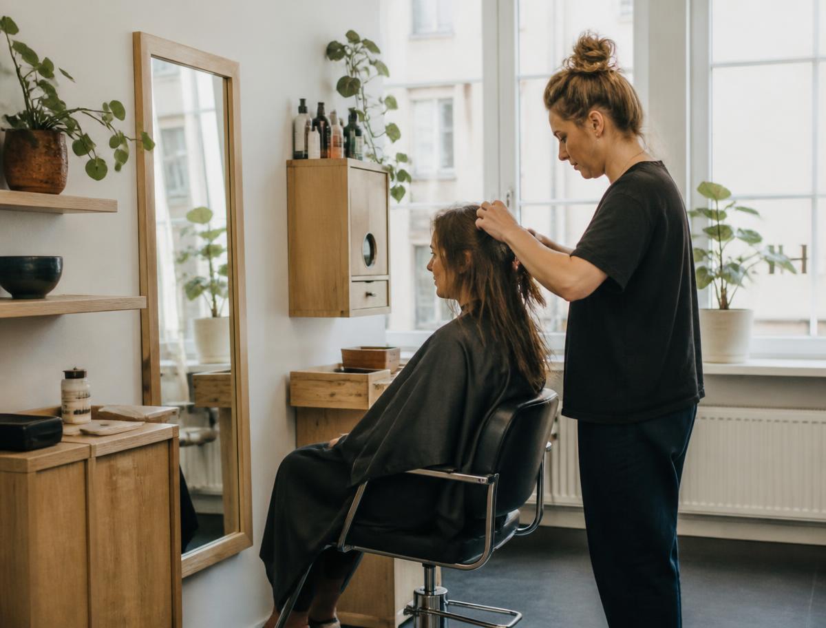 Frisör som stylar en kunds hår i en ljus, personlig salong med ekdetaljer och dagsljus.